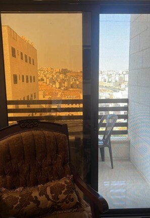 A room with a view of a cityscape through a window, a chair, and a balcony with a chair. - Spacious 3BR Amman Stay with Balcony & Free Parking (Amman)