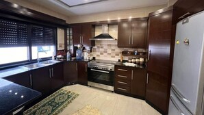 A modern kitchen with dark wooden cabinets, a stainless steel refrigerator, and a built-in oven. - Spacious 3BR Amman Stay with Balcony & Free Parking (Amman)