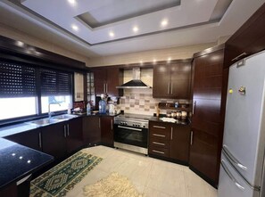 A modern kitchen with dark wooden cabinets, a stainless steel refrigerator, and a built-in oven. - Spacious 3BR Amman Stay with Balcony & Free Parking (Amman)