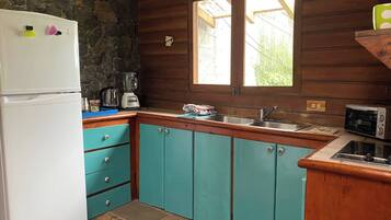 A compact kitchen with a stone wall, a white refrigerator, teal cabinets, a sink, and a window with a view.