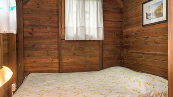 A wooden cabin room with a bed, a window with a curtain, and a framed picture on the wall.