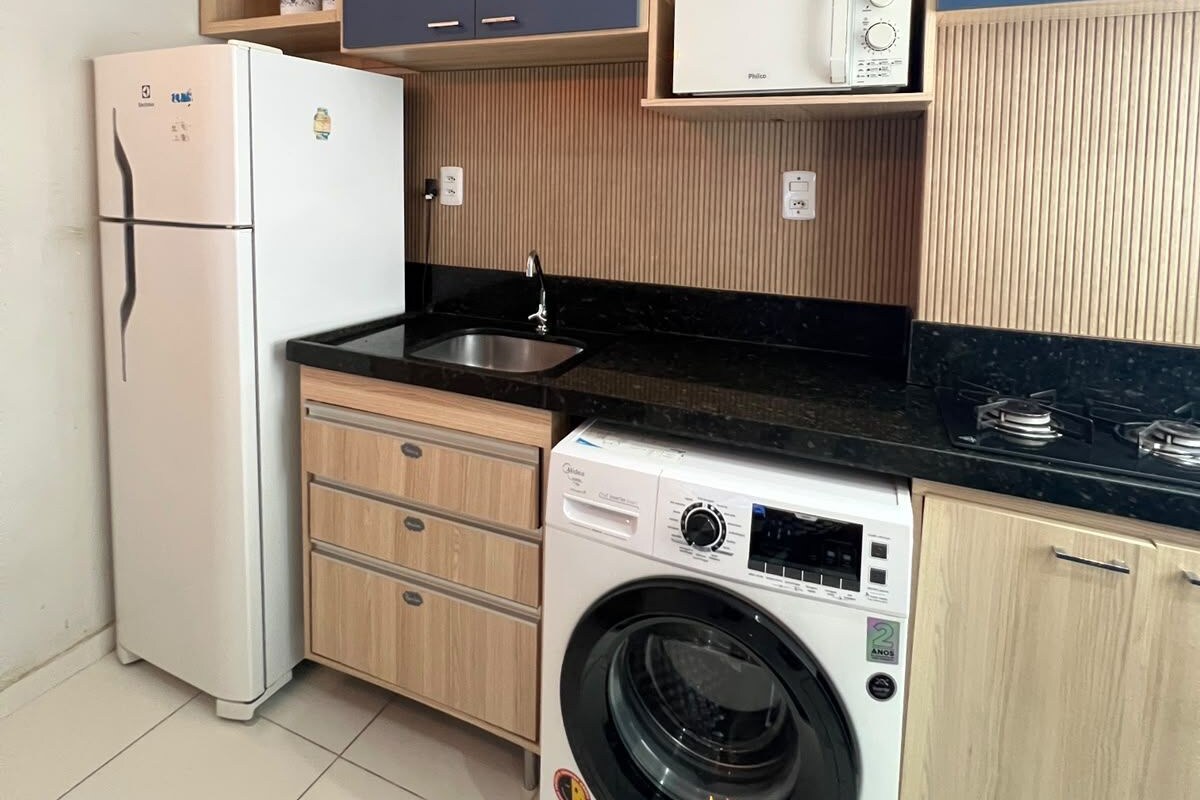 A compact kitchen with a refrigerator, microwave, sink, and washing machine.