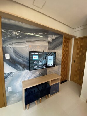 A flat-screen TV mounted on a wall with a marble-like design, a wooden bench below, and a door to the right. - 302 - 2 Quartos Encatador (Belém)