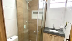 A modern bathroom with a glass-enclosed shower, a toilet, and a sink with a countertop. - 302 - 2 Quartos Encatador (Belém)