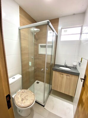 Un baño moderno con ducha envuelta en cristal, inodoro y lavamanos con encimera.