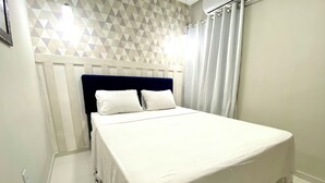 A neatly made bed with white linens in a room with a geometric patterned wall and a dark blue headboard. - 302 - 2 Quartos Encatador (Belém)