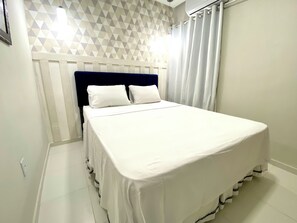 Una cama bien tendida con sábanas blancas en una habitación con pared de estampado geométrico y cabecera azul oscuro.