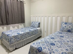 A bedroom with two beds, each with a patterned bedspread, a bedside table, and a curtain. - 302 - 2 Quartos Encatador (Belém)