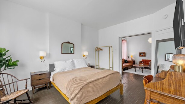 A hotel room with a bed, bedside table, lamp, chair, and a mirror. - NEW! Best Value, Spacious, 1BD, Near Barnes, Nurse Approved! (St. Louis)