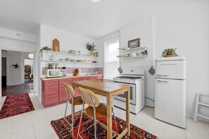 Eine moderne Küche mit rosa Schränken, einem Holztisch und einem weißen Kühlschrank.