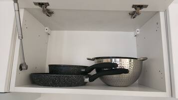 A kitchen cabinet with a metal pot, a frying pan, and a colander.