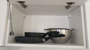 Een keukenkastje met een metalen pot, een koekenpan en een vergiet.