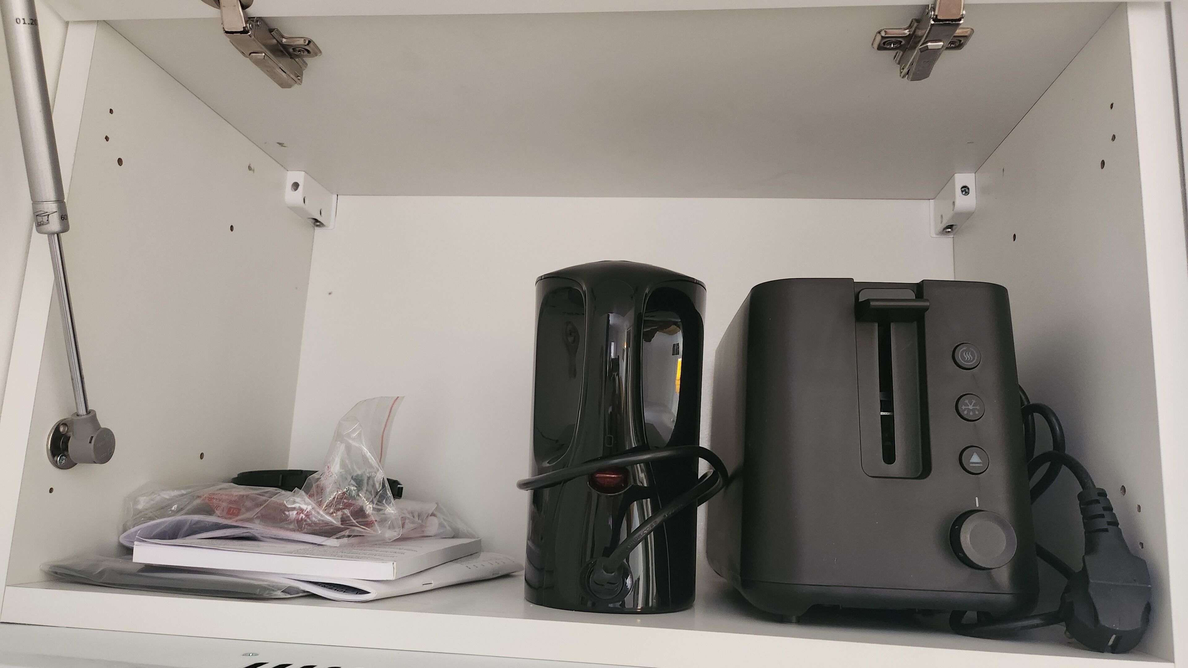 Een wit schap met een laptop, een zwart cilindrisch object en een zwart elektronisch apparaat met snoer.