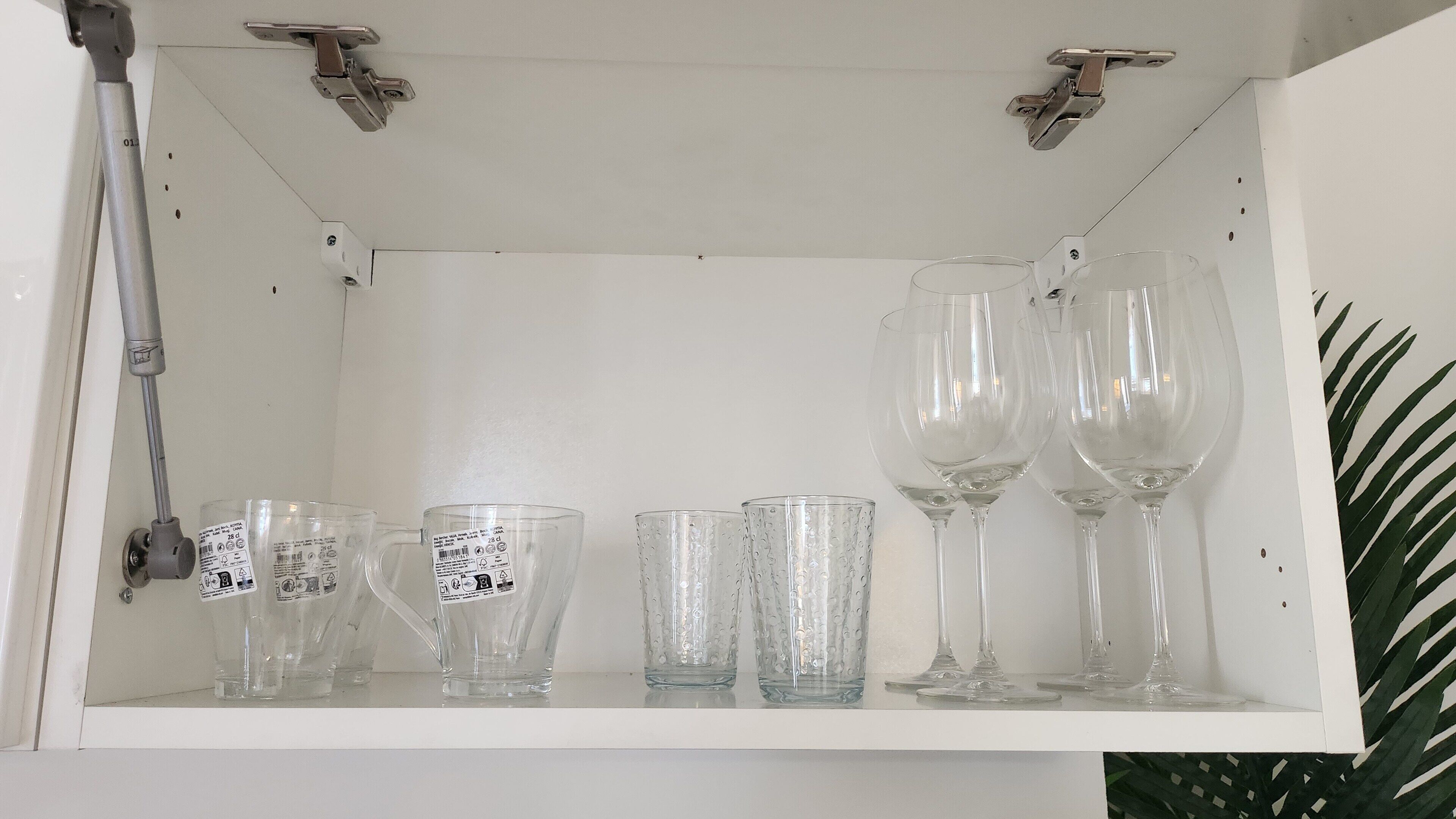 Une étagère blanche sur laquelle sont disposés divers objets en verre, notamment des verres à vin et des verres à cocktail.