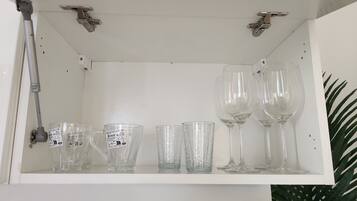 Une étagère blanche sur laquelle sont disposés divers objets en verre, notamment des verres à vin et des verres à cocktail.