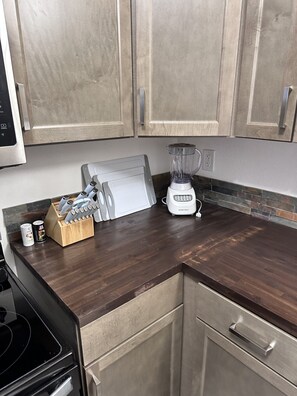 A kitchen with wooden cabinets, a countertop, a blender, a knife block, and a stove. - Elegant & Cozy 2BR Apartment with Chugach Mountain Views #2 (Anchorage)