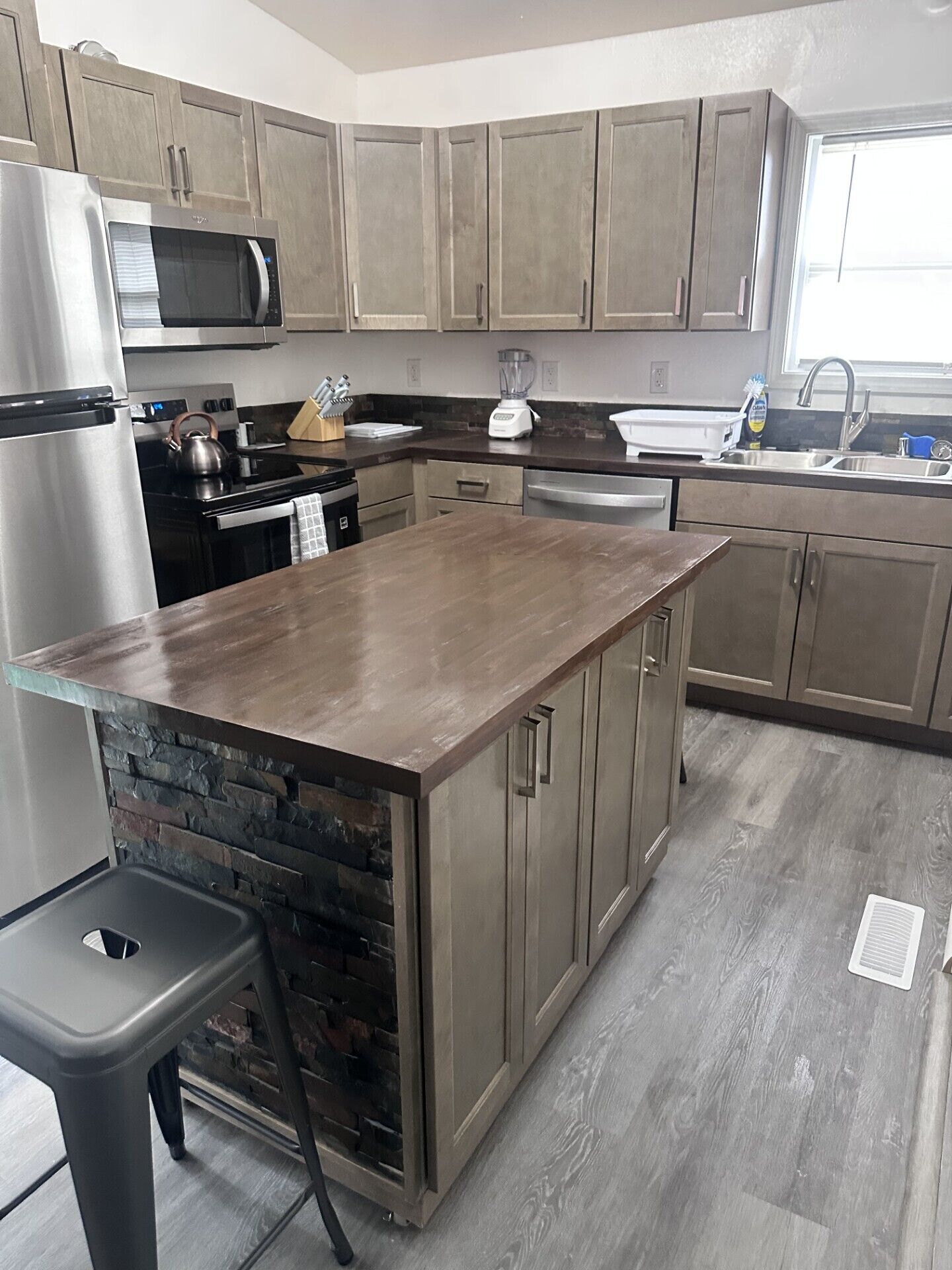 Uma cozinha com ilha central, eletrodomésticos de aço inoxidável e armários de madeira clara.