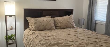 A bedroom with a bed, bedside lamps, a bedside plant, and a motivational quote on the wall.