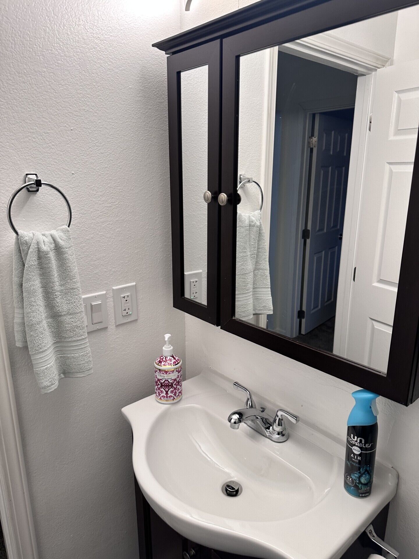 Une salle de bain avec un lavabo blanc, un miroir à cadre noir et un porte-serviettes sur lequel est posée une serviette blanche.