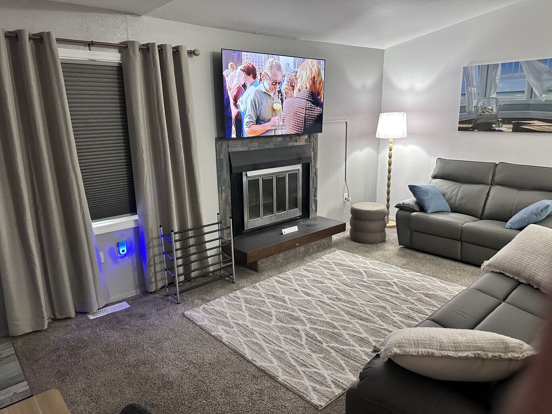 A living room with a fireplace, a television mounted above it, a sofa, and a lamp.