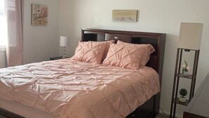 Ein Schlafzimmer mit einem Bett, einem Nachttisch, einer Lampe, einer Wanddekoration und einer kleinen Pflanze auf einem Regal.