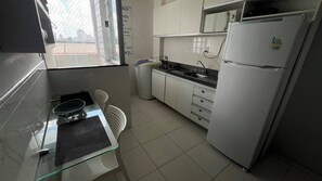 A compact kitchen with white cabinets, a refrigerator, a sink, and a dining area with a chair and table. - 304 2 Qtos - Estilo e Confortável (Belém)