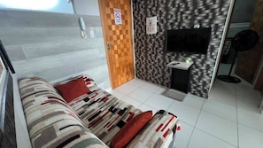 A room with a bed, a TV, a small table with a plant, and a wall-mounted fan. - 304 2 Qtos - Estilo e Confortável (Belém)