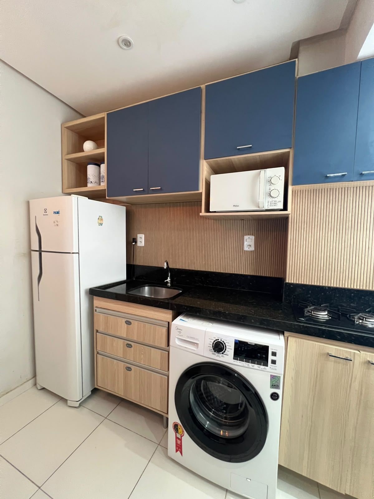 Cocina compacta con refrigerador, microondas, lavamanos y lavadora.