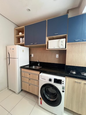 A compact kitchen with a refrigerator, microwave, sink, and washing machine. - 304 2 Qtos - Estilo e Confortável (Belém)