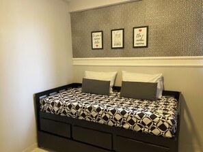 Een bed met een bedspread met geometrisch patroon, een hoofdbord met een decoratief paneel, en drie ingekaderde items aan de muur boven het bed.