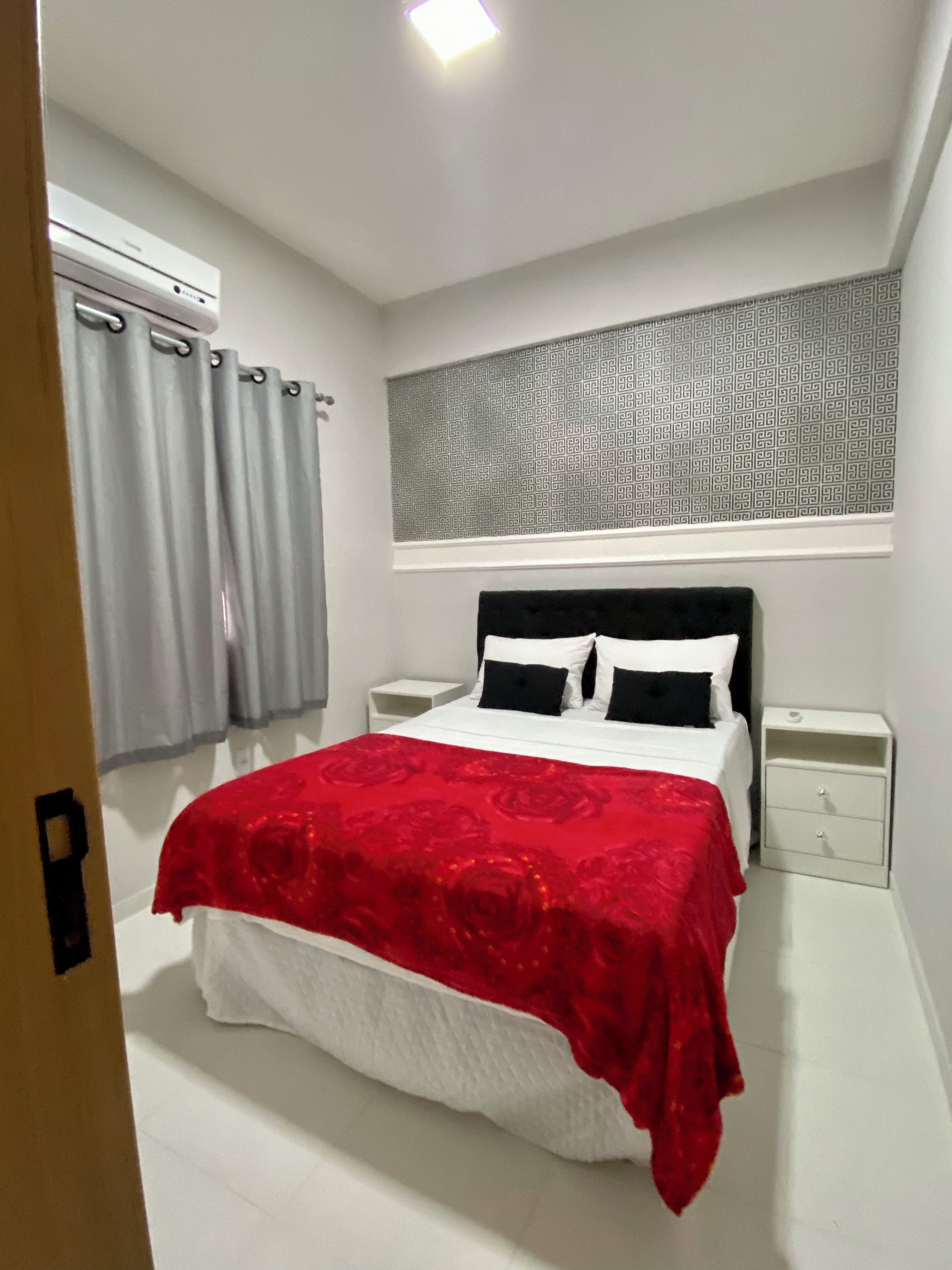 Una camera da letto con un letto, comodini, una finestra con tende e una parete decorata sopra il letto.