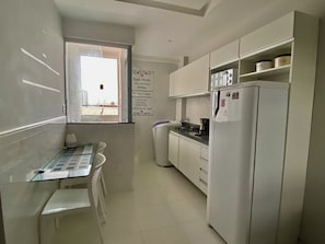 A compact kitchen with white cabinets, a refrigerator, a stove, and a dining table with chairs. - 304 2 Qtos - Estilo e Confortável (Belém)