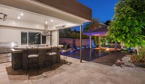 An outdoor kitchen area with a bar and seating, a swimming pool with lighting, and a covered patio with a pergola. - Spacious house with amazing view (West Covina)