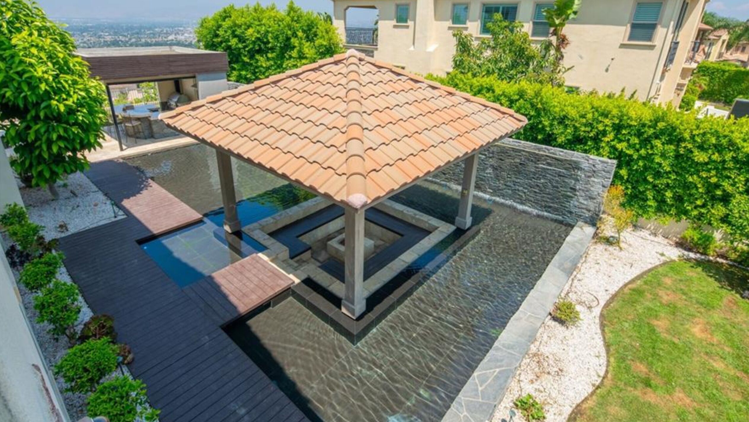 Ein Poolbereich auf dem Dach mit einer Pergola, umgeben von üppiger Vegetation und Blick auf die Stadt.
