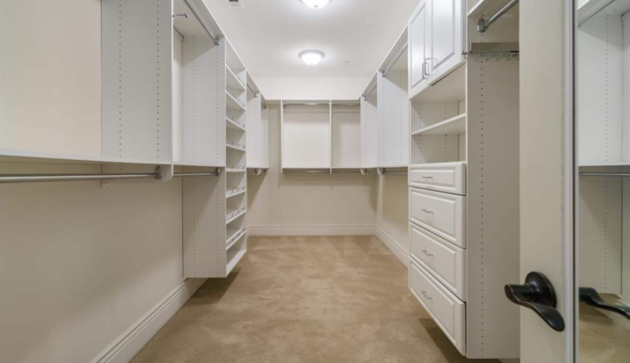 A walk-in closet with open shelving, drawers, and a door with a black handle.