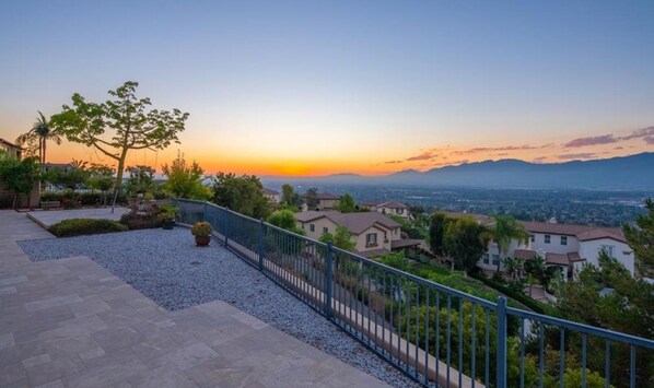 Un quartier résidentiel avec des maisons, un chemin piétonnier pavé et une vue sur les montagnes lointaines au coucher du soleil.