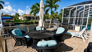 An outdoor patio with a round table, chairs, and an umbrella. - Almare – Gulf Access, Pool, Spa & Boat Dock (Cape Coral)