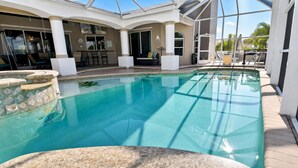 An indoor swimming pool with clear water, surrounded by a covered patio area with seating and a view of the outdoors. - Almare – Gulf Access, Pool, Spa & Boat Dock (Cape Coral)