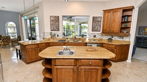 A spacious kitchen with a large island, granite countertops, wooden cabinetry, and a view to the outside. - Almare – Gulf Access, Pool, Spa & Boat Dock (Cape Coral)