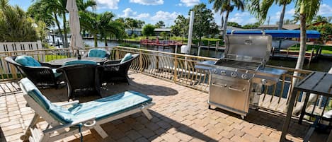 Une terrasse extérieure équipée d’un barbecue, de chaises longues et offrant une vue sur un plan d’eau.