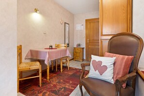 A dining area with a table set for two, a wooden chair with a heart-patterned pillow, and a small cabinet.