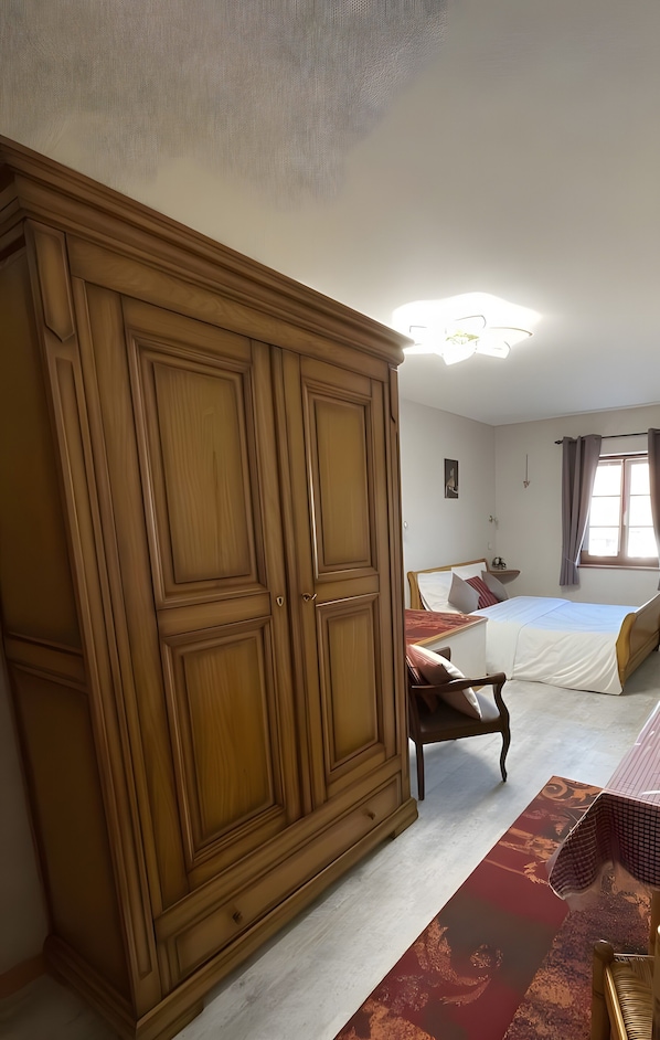 A bedroom with a large wardrobe, a bed with pillows, a bedside table, and a window with curtains.
