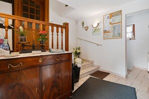Una escalera de madera con barandilla, un mueble de madera con cajones y una pequeña mesa con un jarrón de flores.