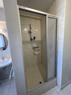 A modern bathroom with a glass-enclosed shower, a sink with a soap dispenser, and a mirror.