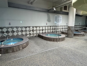 Área de piscina com vários ofurôs, piso em azulejo e placa com as regras do spa.