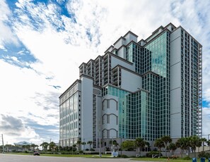 A multi-story building with a modern architectural design, featuring a mix of glass and concrete facades. - Luxury Beachfront + Lazy River-The Oasis at Orange Beach 1001 (Orange Beach)