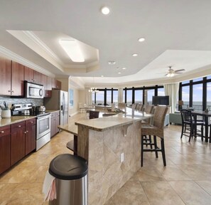 A modern kitchen with a central island, stainless steel appliances, and a large window overlooking a scenic view. - Luxury Beachfront + Lazy River-The Oasis at Orange Beach 1001 (Orange Beach)