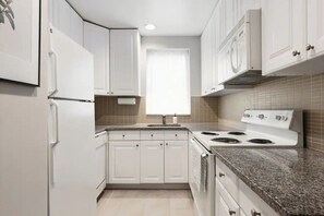 A kitchen with white cabinets, a stove, and a sink. - Bayard | One-Bedroom King | Turtle Bay | Free Breakfast (New York)