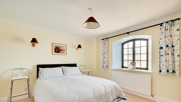 A bedroom with a bed, two bedside lamps, a window with curtains, a radiator, and a small picture on the wall. - 1 Bed in Wells-next-the-Sea (oc-591) (Wells-next-the-Sea)