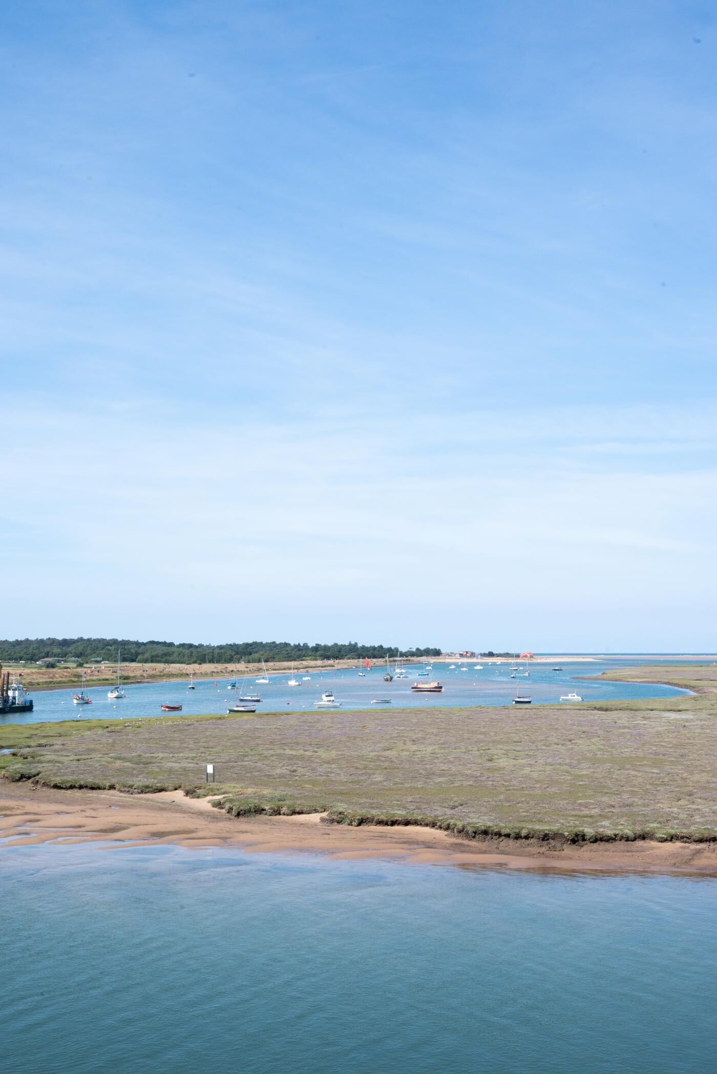A coastal landscape with boats anchored in a calm bay, a sandy beach, and a distant shoreline with vegetation.
